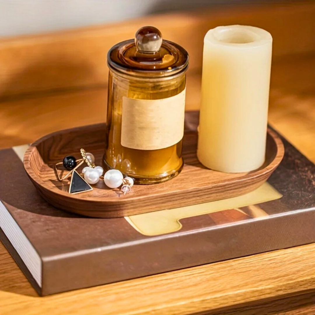 Jewelry, candle, and amber jar styled on walnut Mokura tray atop a hardcover book