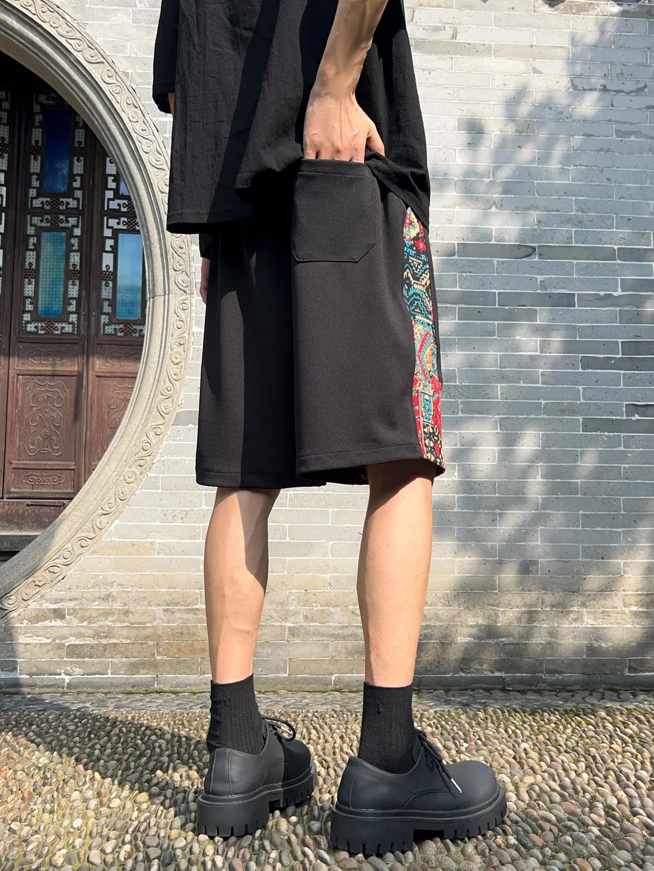 Back view of black woven patchwork shorts showing pocket and side pattern