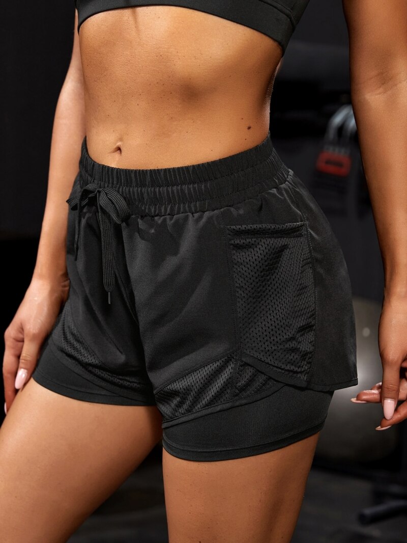 Black athletic shorts with deep pocket, gym background. Side View