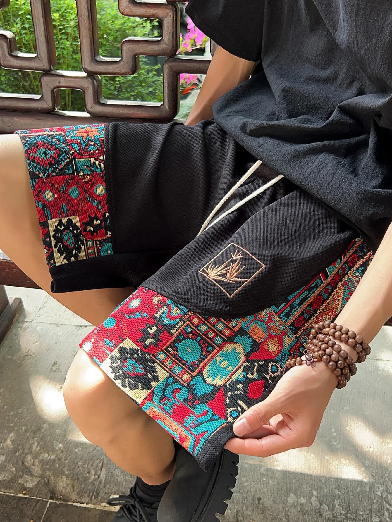 Black ethnic patchwork shorts with red and teal woven panels, seated view with drawstring detail