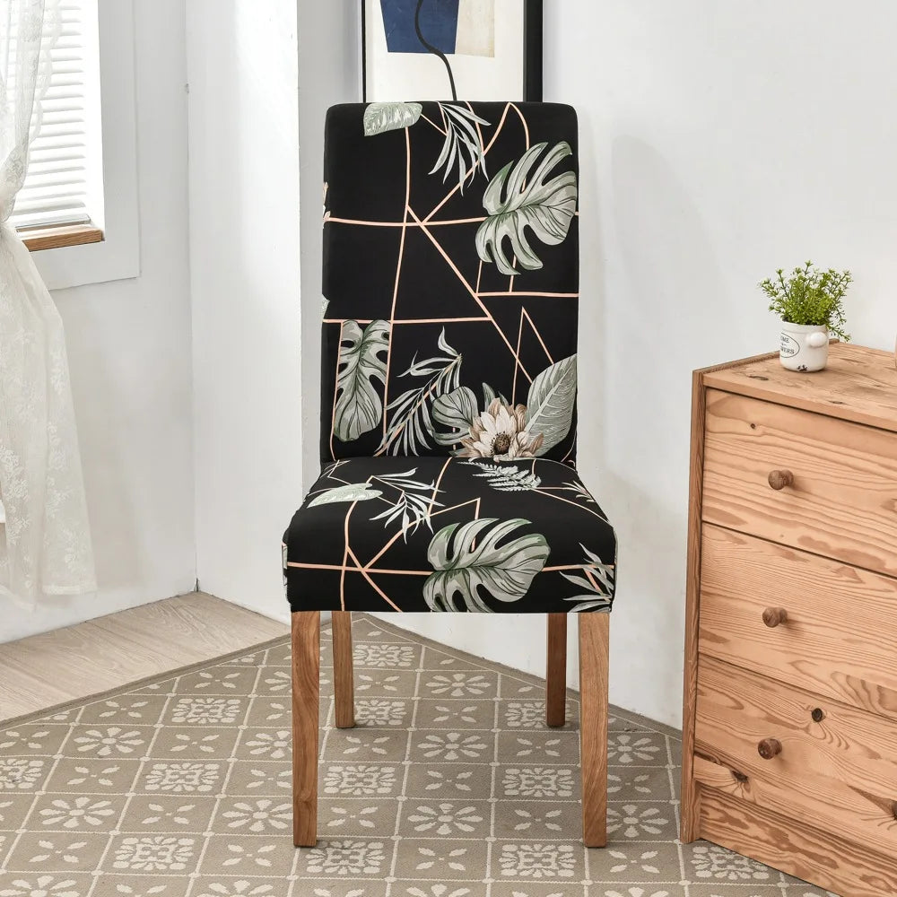 Black stretch chair cover with green monstera and floral prints on wood-frame dining chair