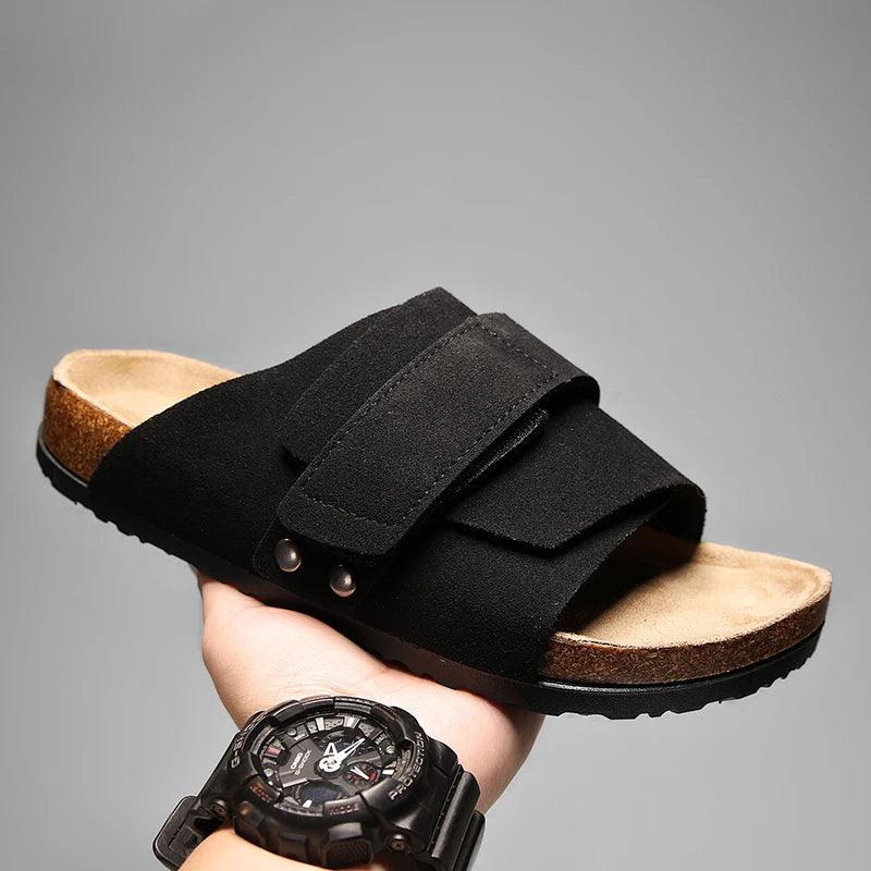 Black suede men’s sandal with dual straps and textured rubber sole, held in hand