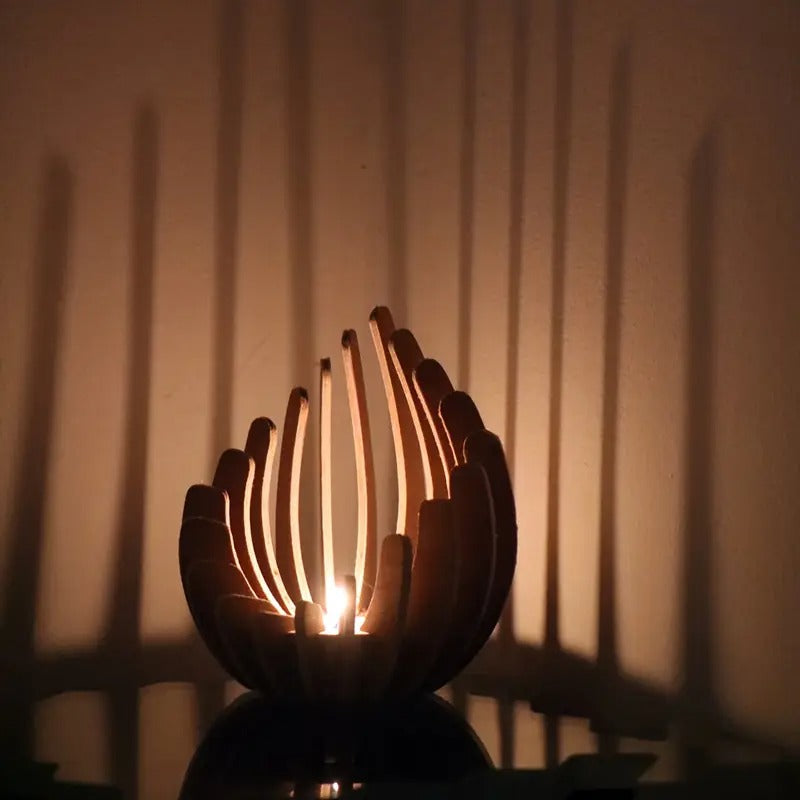 Candlelight glowing through lotus-shaped wooden holder casting tall shadows