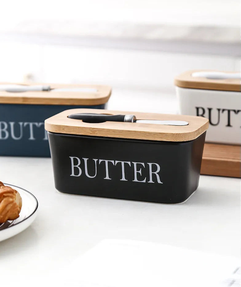 Colorful ceramic butter dishes in black, white, and nanvy blue with bamboo lids and croissant on side