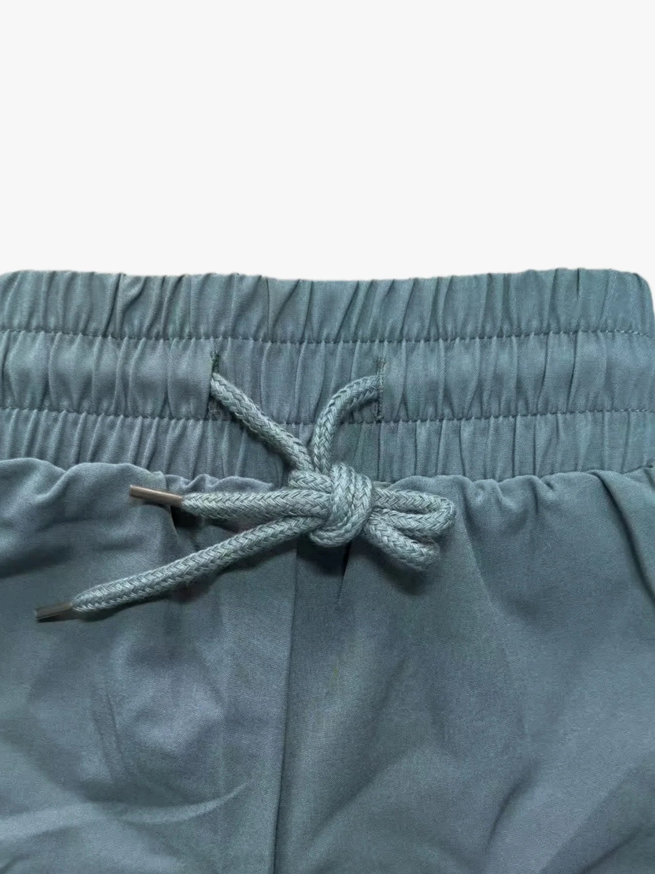 Detailed close-up of teal workout shorts waistband and braided drawstring tie, front view