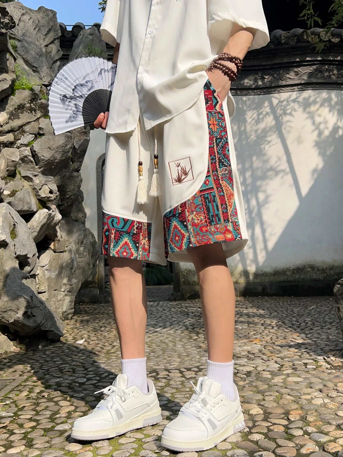 Front view of white ethnic patchwork shorts with colorful woven panels and tassel drawstring