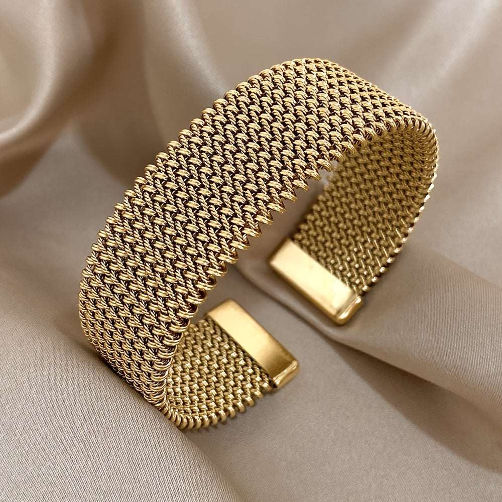 Gold woven stainless steel bracelet on beige satin background, angled side view