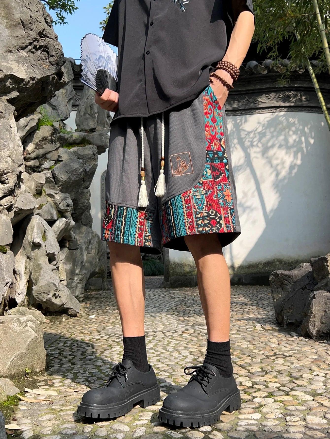 Gray ethnic patchwork shorts with tassel drawstring, styled with black shirt and chunky shoes