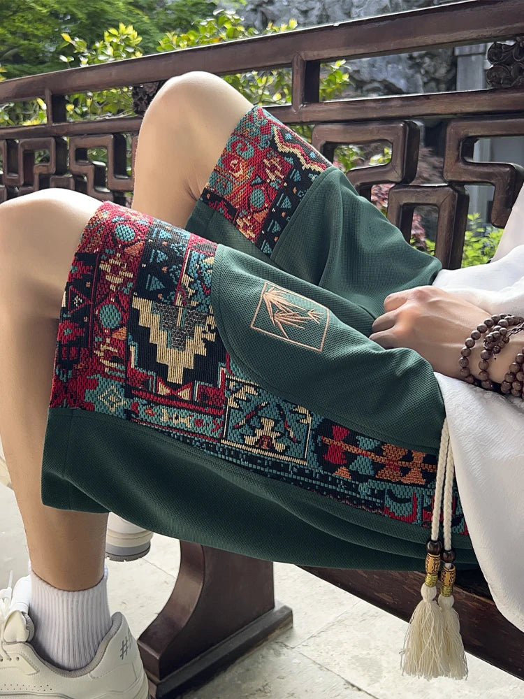 Green embroidered ethnic shorts with side woven patterns, close-up seated view with tassels