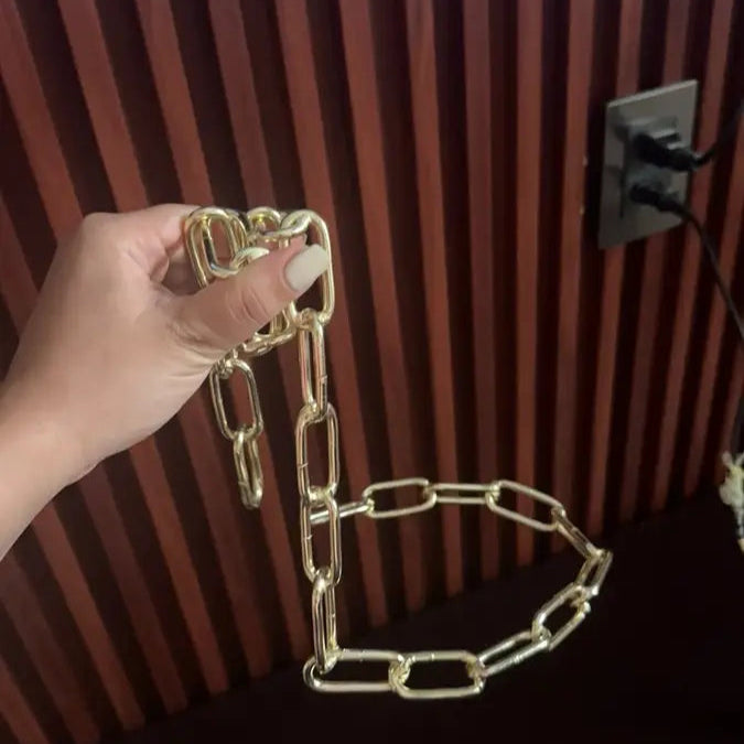 Hand holding golden chain wine holder near red striped wall