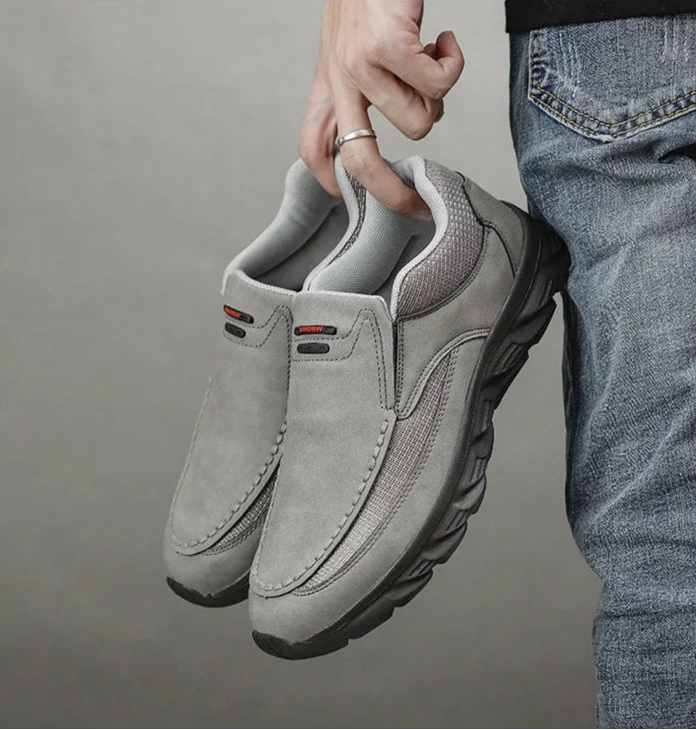 Hand holding pair of grey leather casual loafers against dark background