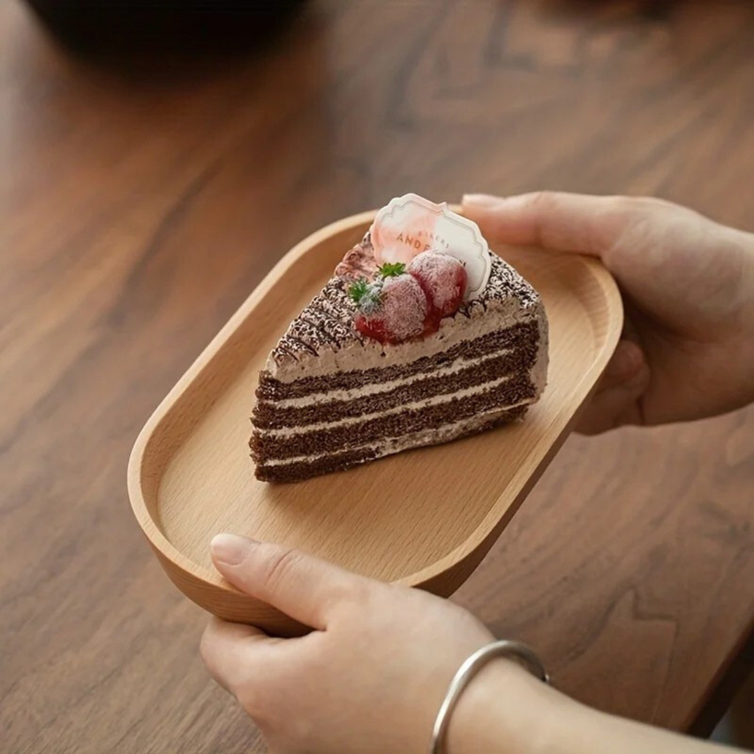 Hands holding beech Mokura solid wood tray with layered chocolate cake slice on dark wood table