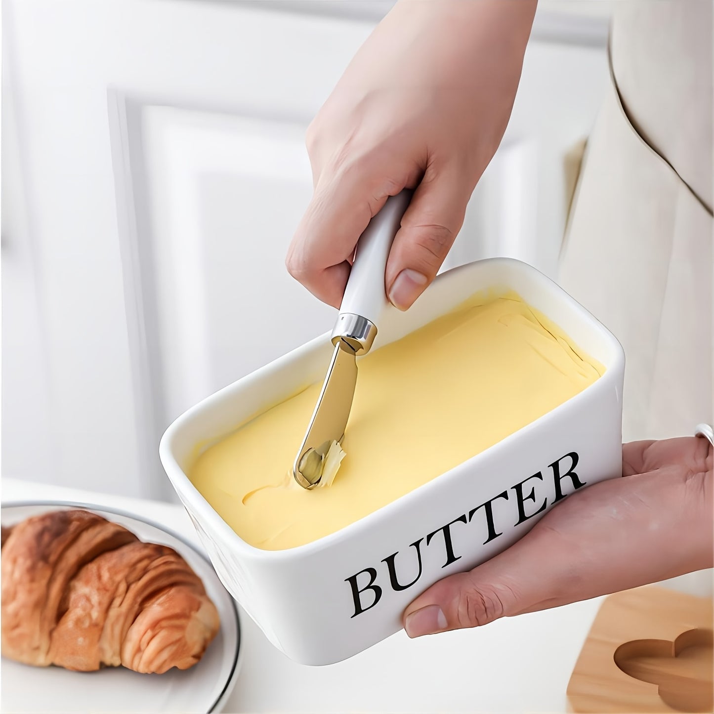 Large ceramic butter dish in white with bamboo lid and built-in knife, shown holding a full block of supermarket butter while spreading