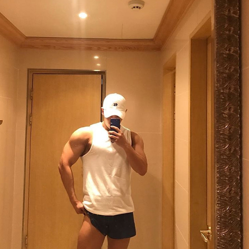 Man posing in white mesh workout tank top and shorts in well-lit bathroom