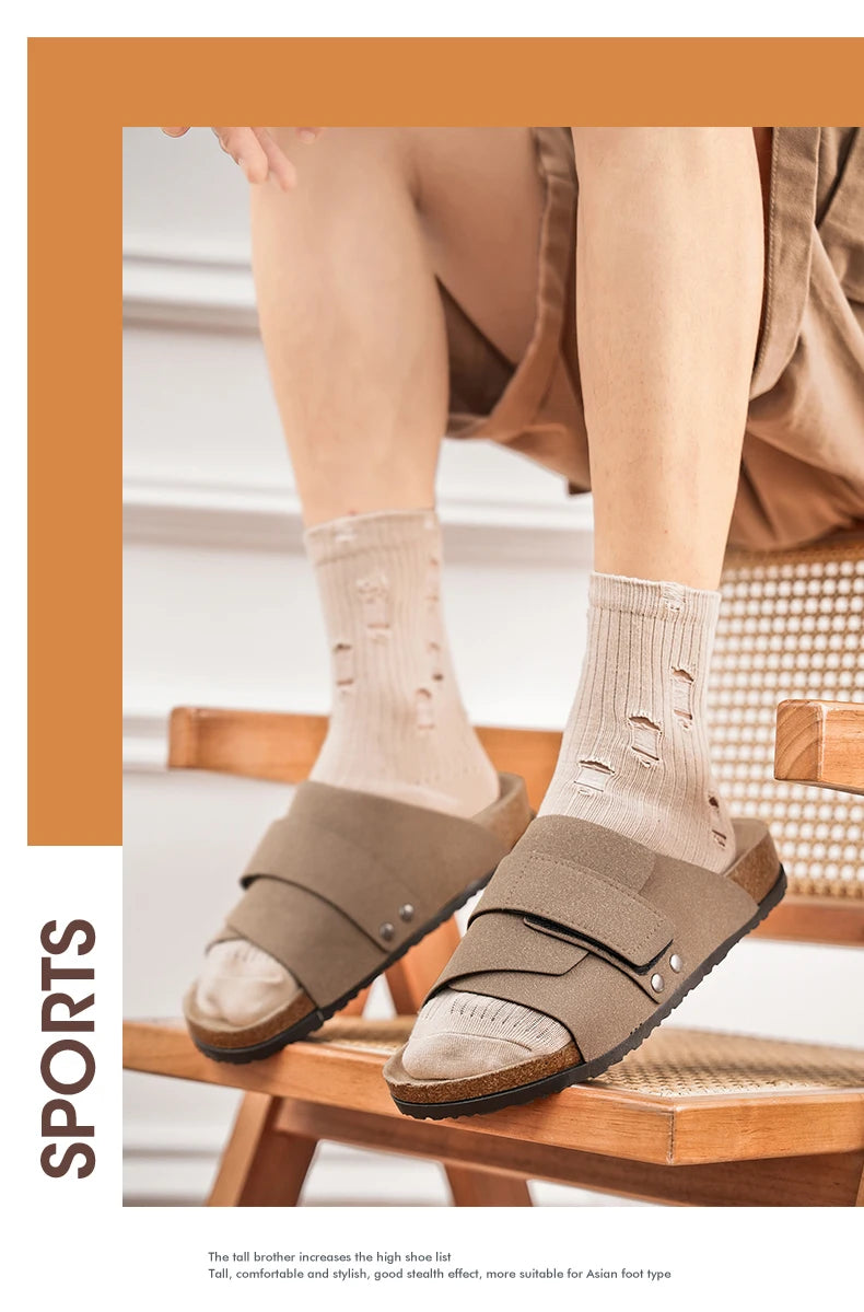 Man wearing black suede slide sandals with cork footbed and beige socks, lifestyle view on wood floor