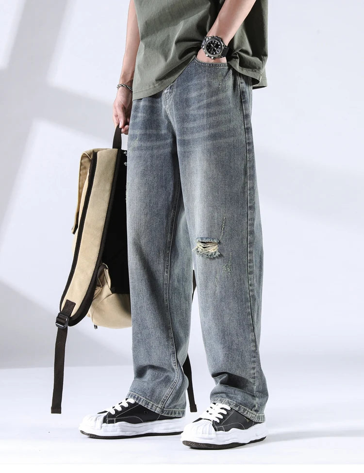 Men’s ice-wash distressed jeans with frayed rip and backpack, angled side view