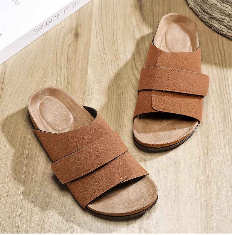 Pair of brown suede slide sandals placed on wooden floor, top view