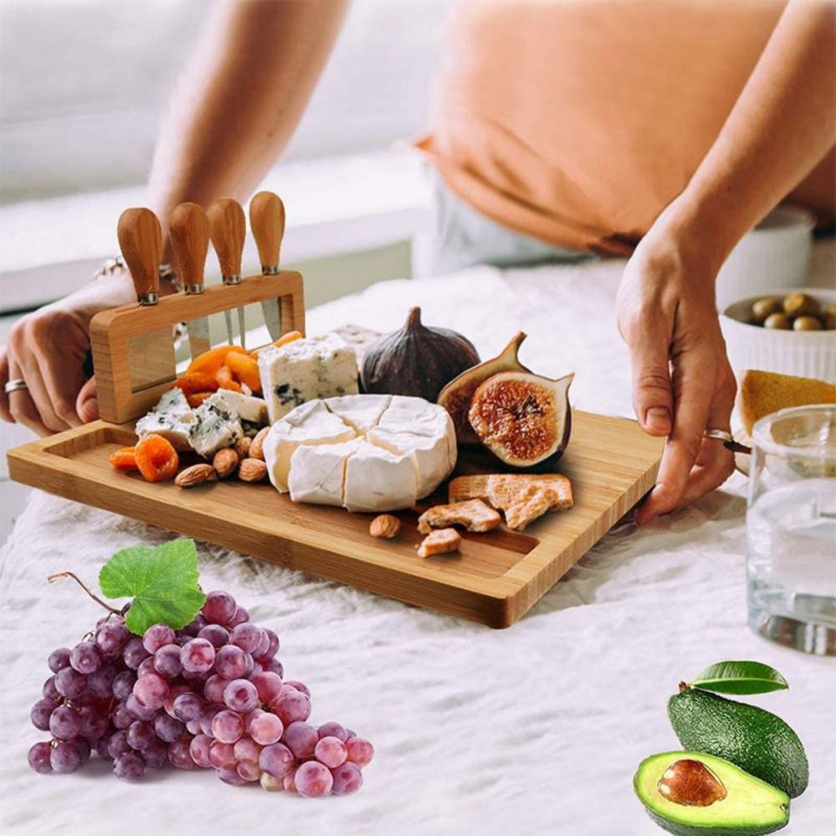 Person serving wooden charcuterie board with cheese and figs in a cozy home setting