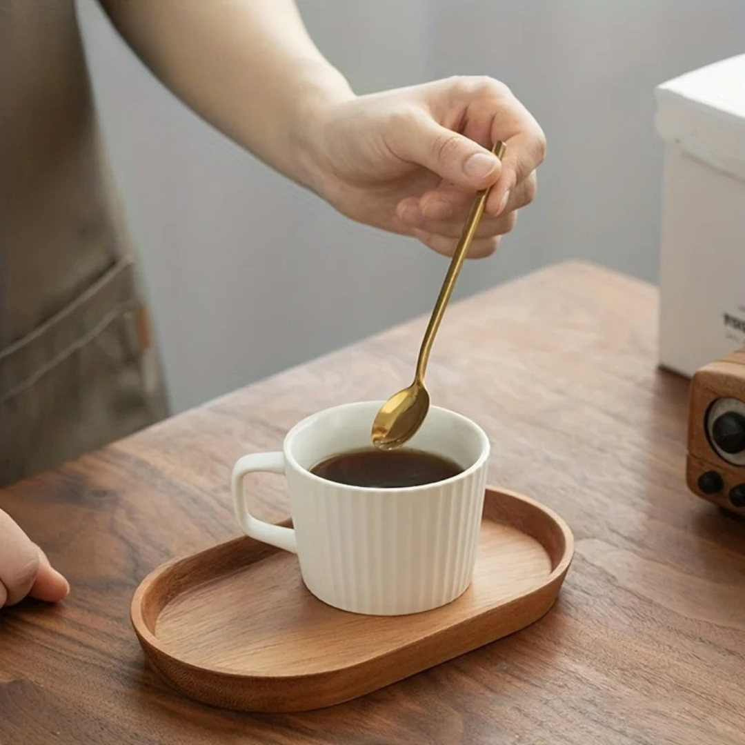 Person stirring coffee in white ribbed mug on medium-tone Mokura tray with gold spoon