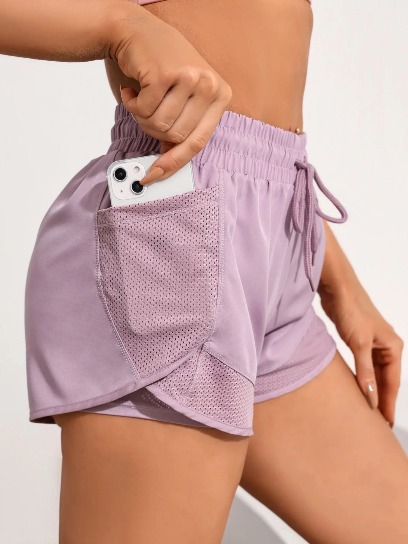 Phone placed in lavender mesh side pocket on women's workout shorts, secure storage focus