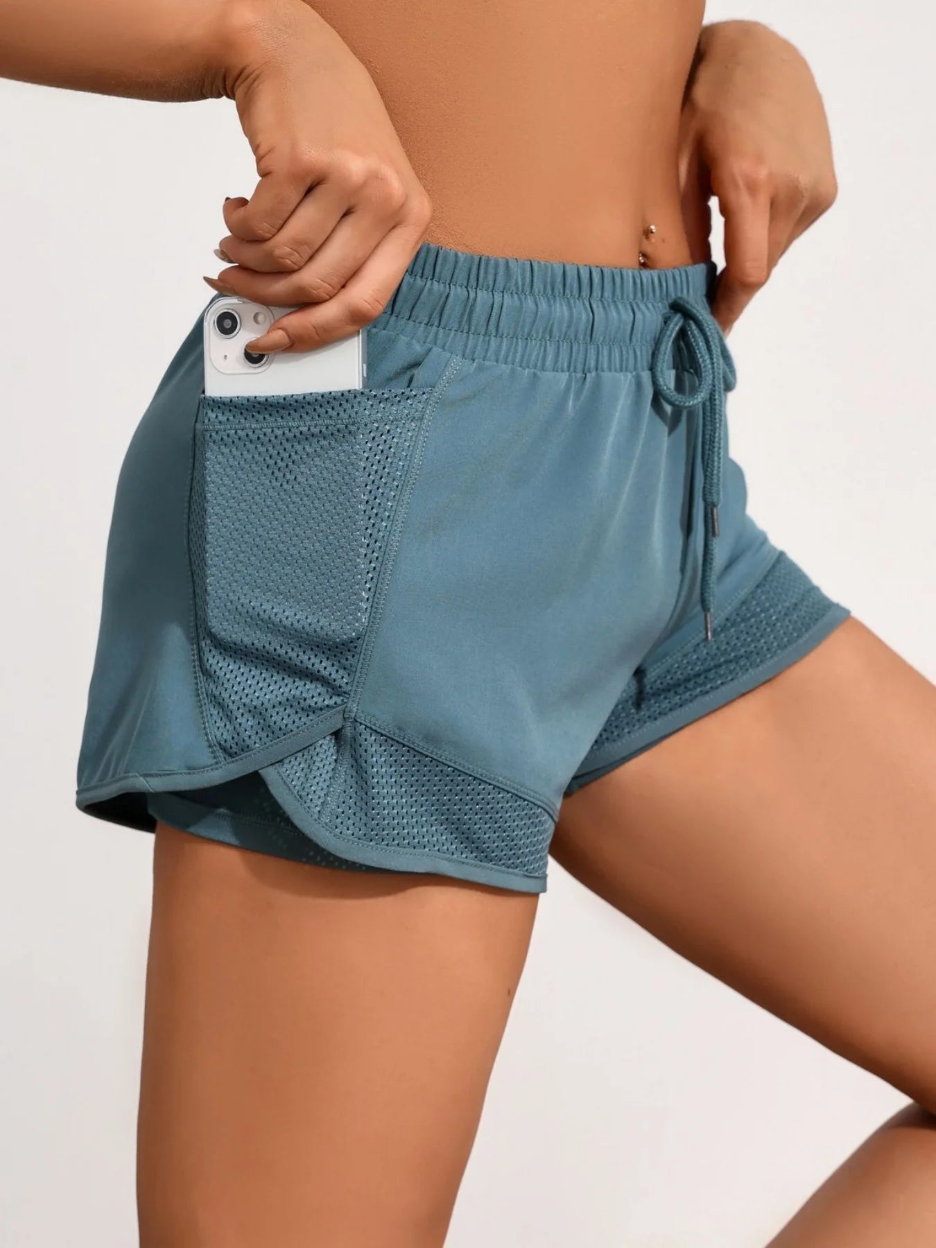 Phone placed in teal mesh side pocket on women's workout shorts, secure storage focus