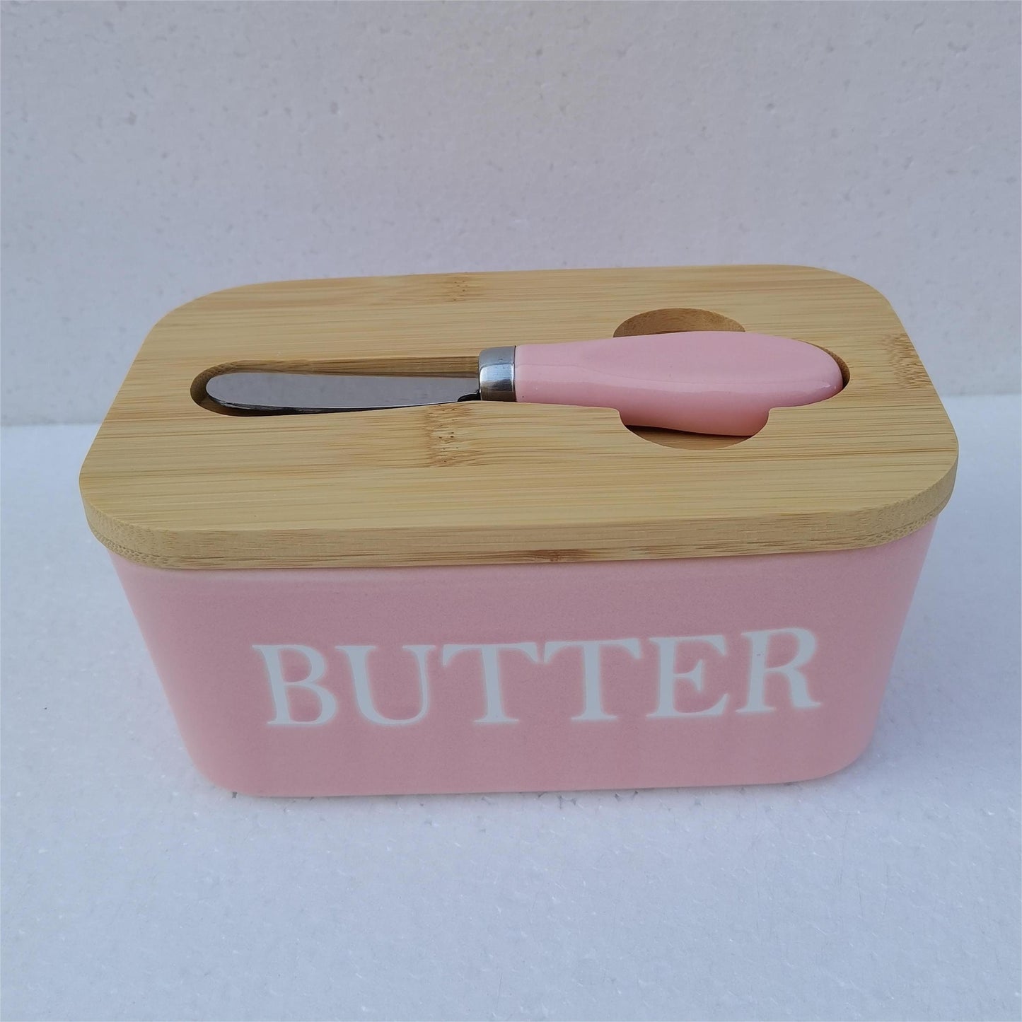 Pink ceramic butter dish with bamboo lid and white spreader, side view