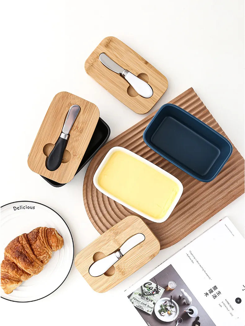 Set of colorful ceramic butter dishes in yellow, teal, white, and black with bamboo lids and spreaders