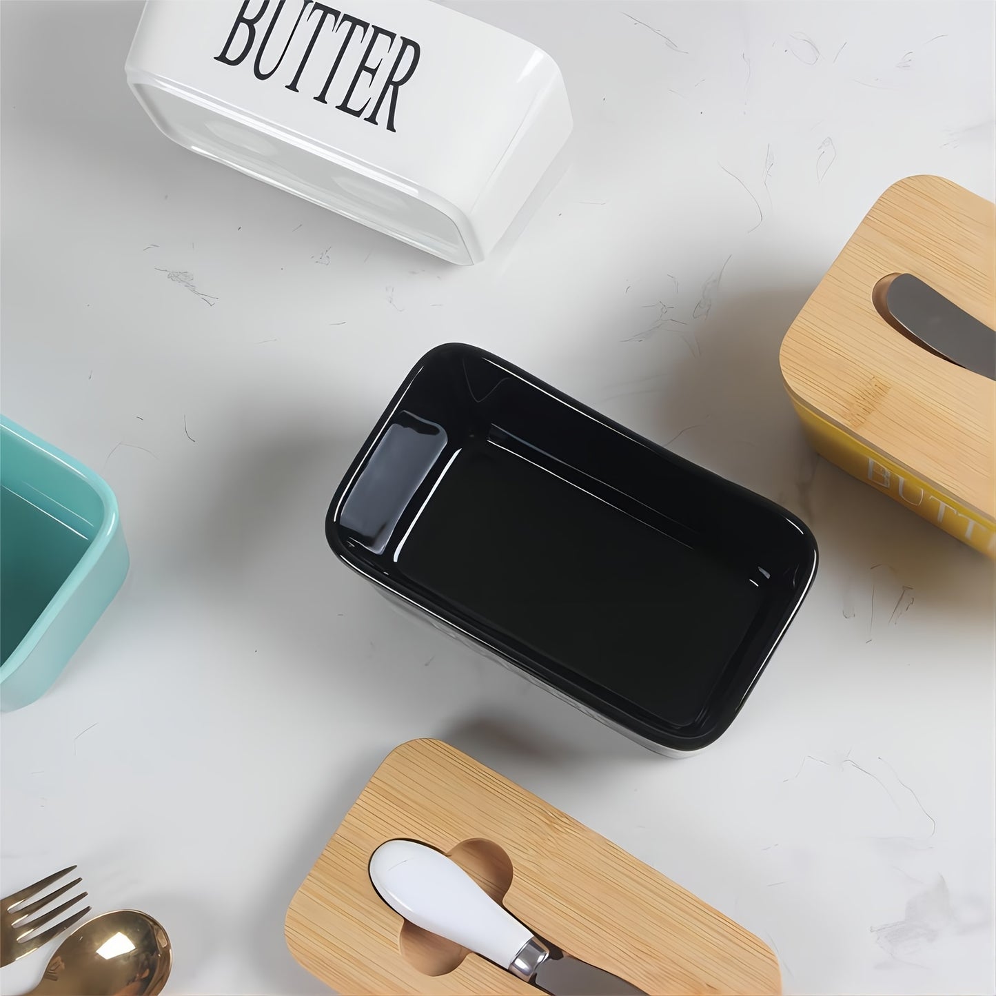 Set of colorful ceramic butter dishes in yellow, teal, white, and black with bamboo lids and spreaders, top view