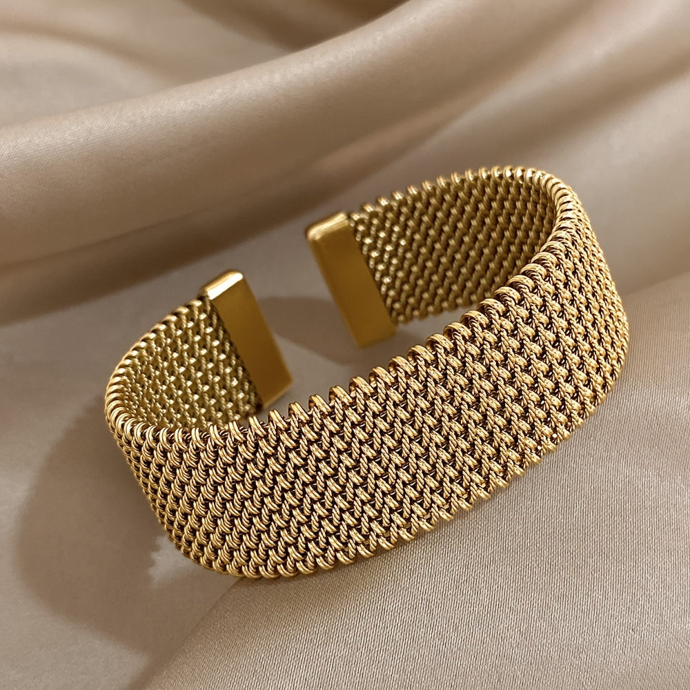 Side angle of gold stainless steel open cuff bracelet resting on satin