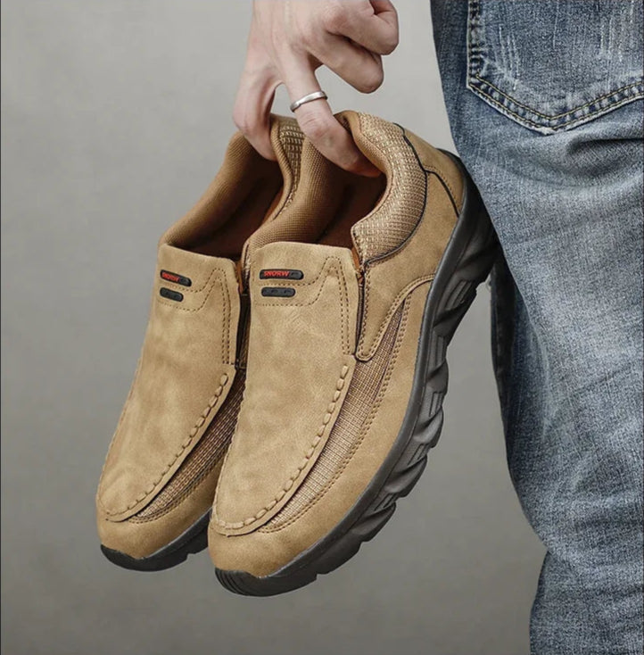 Tan leather loafers held in hand, showcasing soft upper and rugged sole