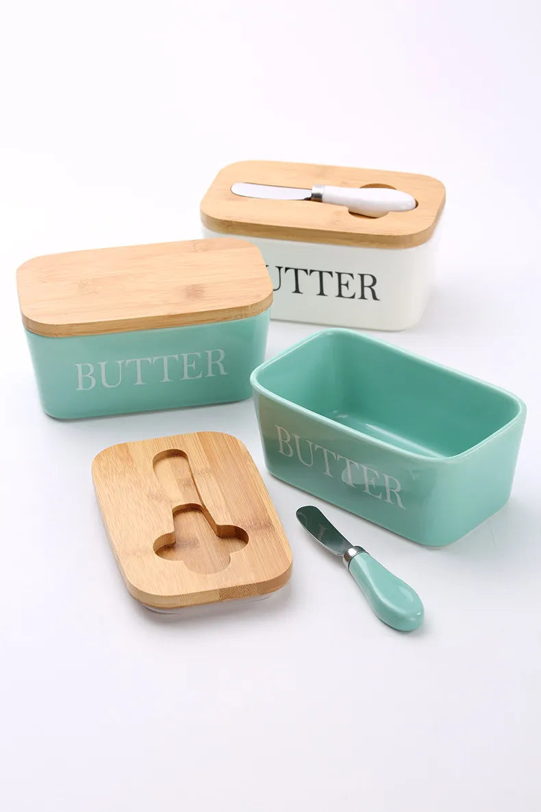 Teel and white ceramic butter dish with butter block beside a croissant on plate and stainless steel spreader