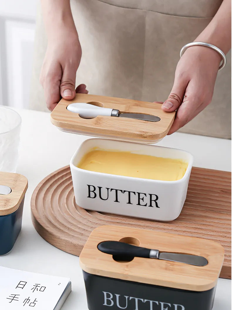 White ceramic butter dish with butter block beside a croissant on plate and stainless steel