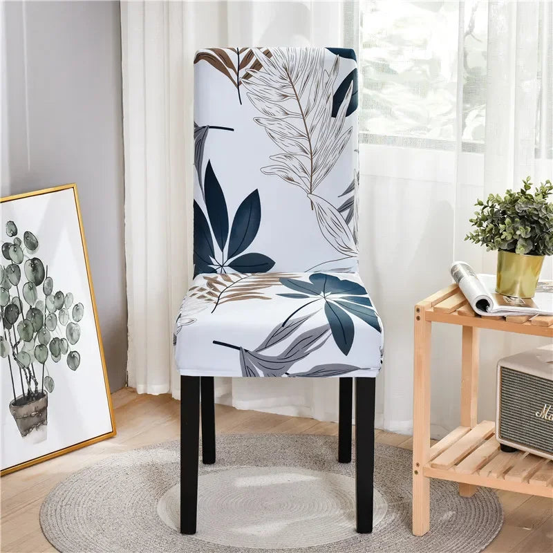 White stretch chair cover with blue and taupe tropical leaf pattern in sunlit modern room