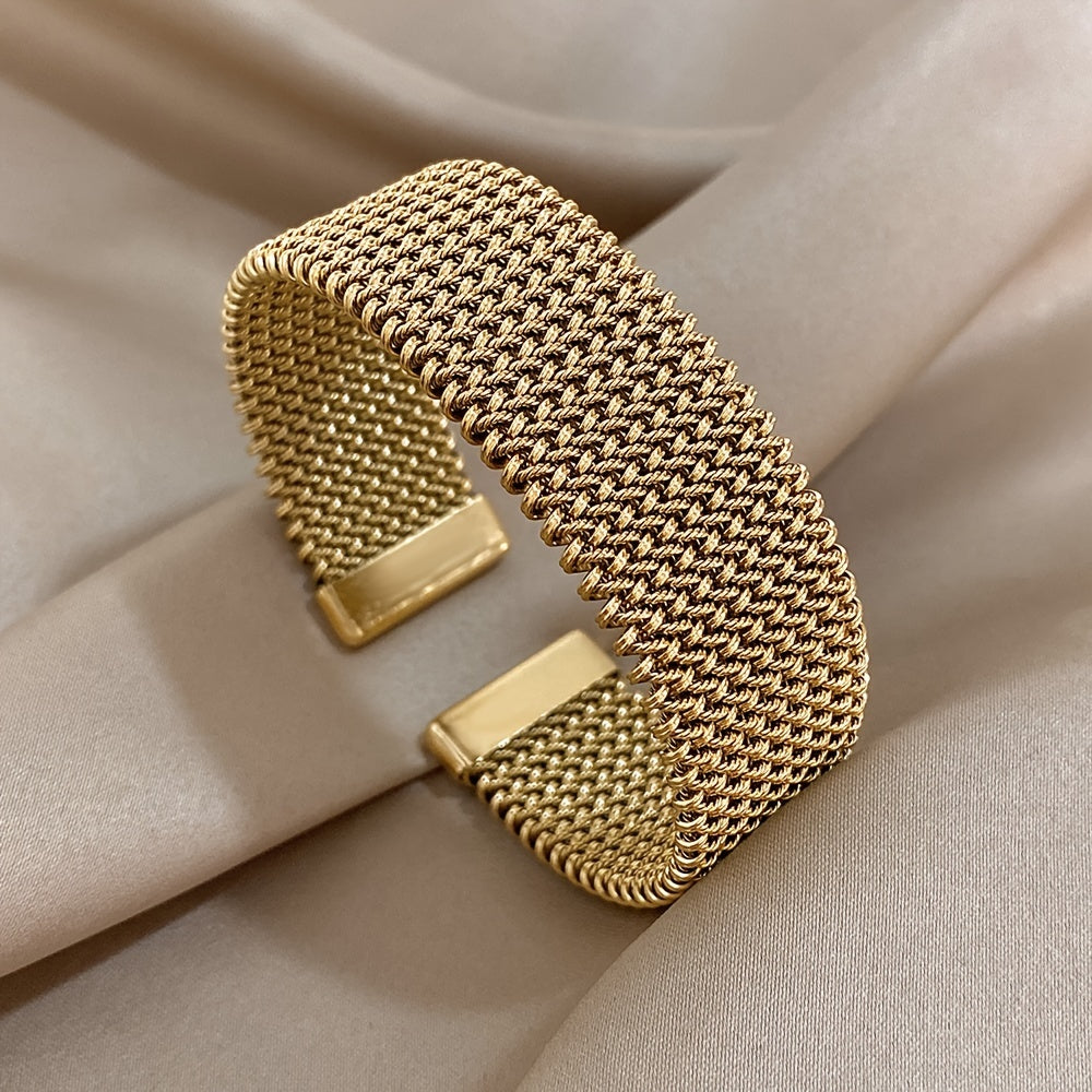 Wide gold mesh cuff bracelet on beige fabric, top view