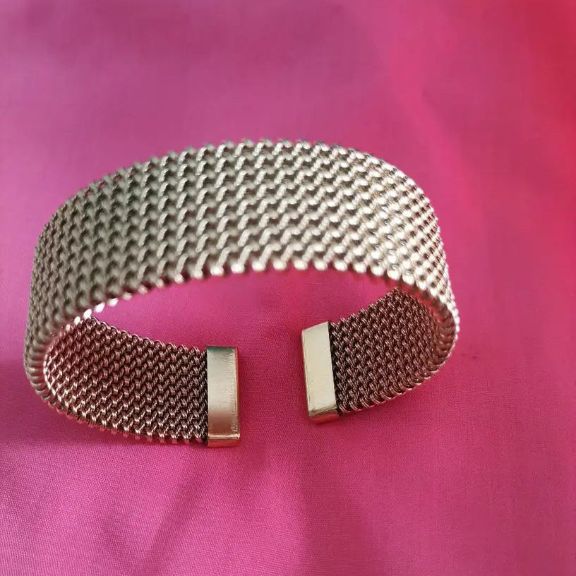 Wide gold mesh cuff bracelet on pink fabric, top view