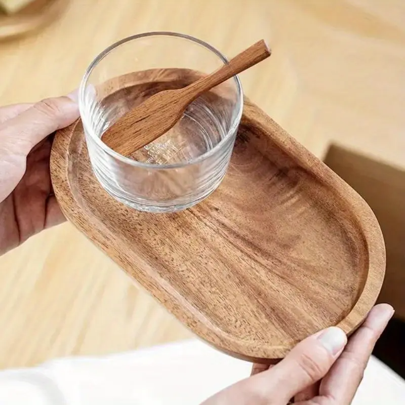Wooden tray with ceramic teacups and decorative candle, styled on white fabric with dried pine