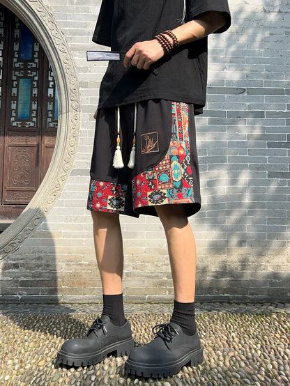 Angled front view of black embroidered patchwork shorts styled with fan and beads