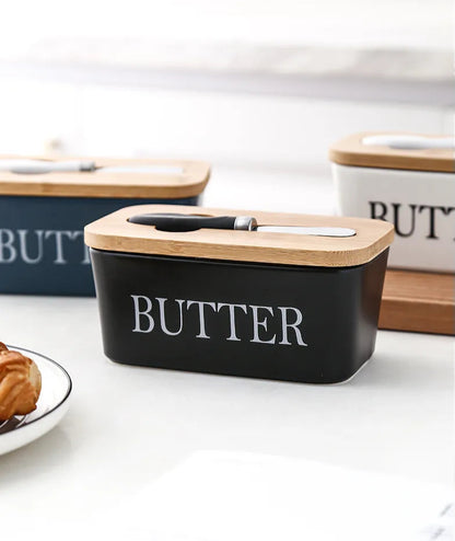 
Colorful ceramic butter dishes in black, white, and nanvy blue with bamboo lids and croissant on side