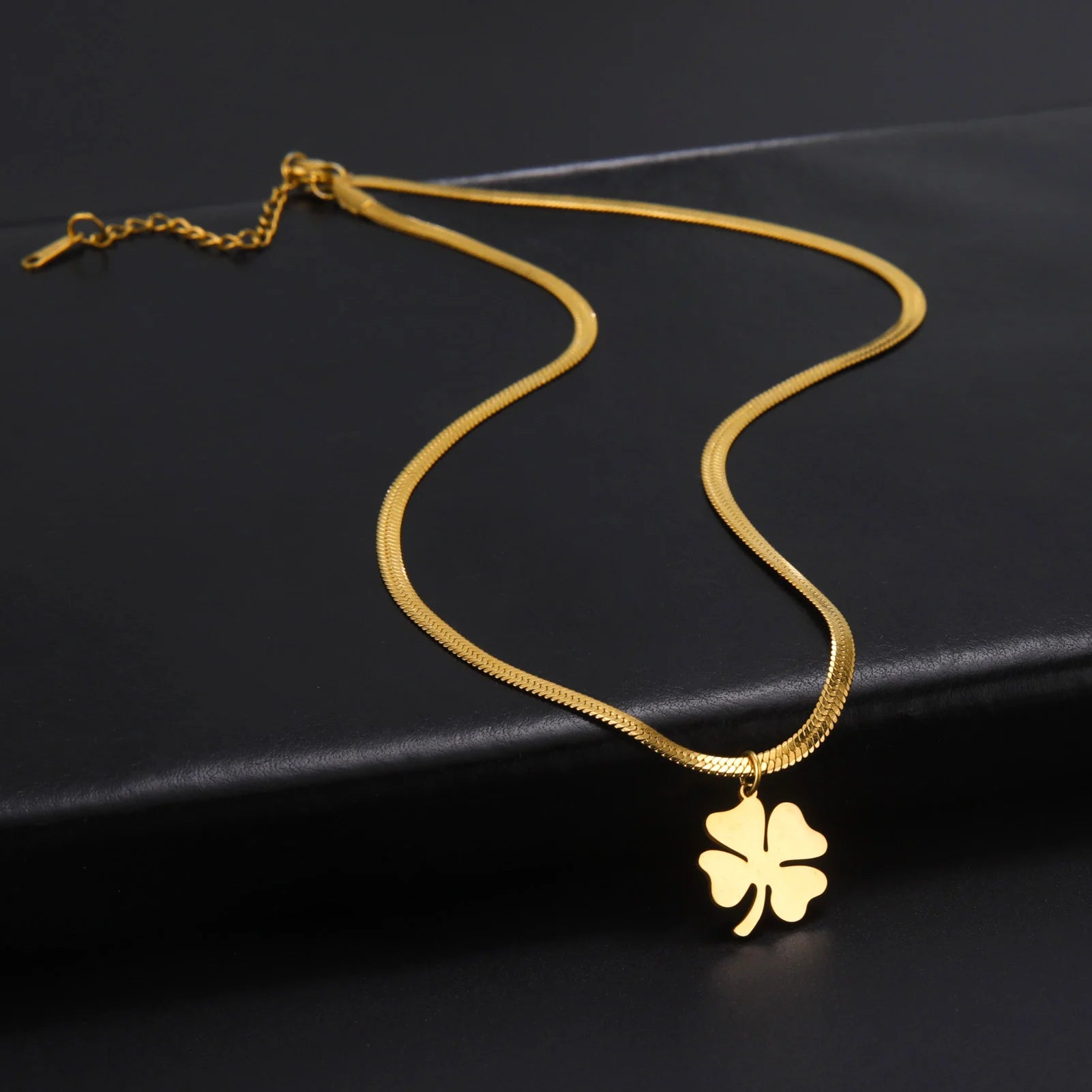 Extended view of gold clover necklace with chain clasp, flat lay on black surface