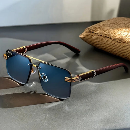 Frameless sunglasses with blue gradient lenses and gold-trimmed temples, styled on grey tabletop beside straw pouch