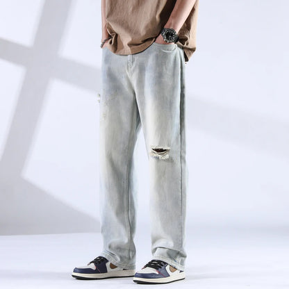Front view of light ice-wash distressed jeans with knee rip and worn-in look, paired with sneakers