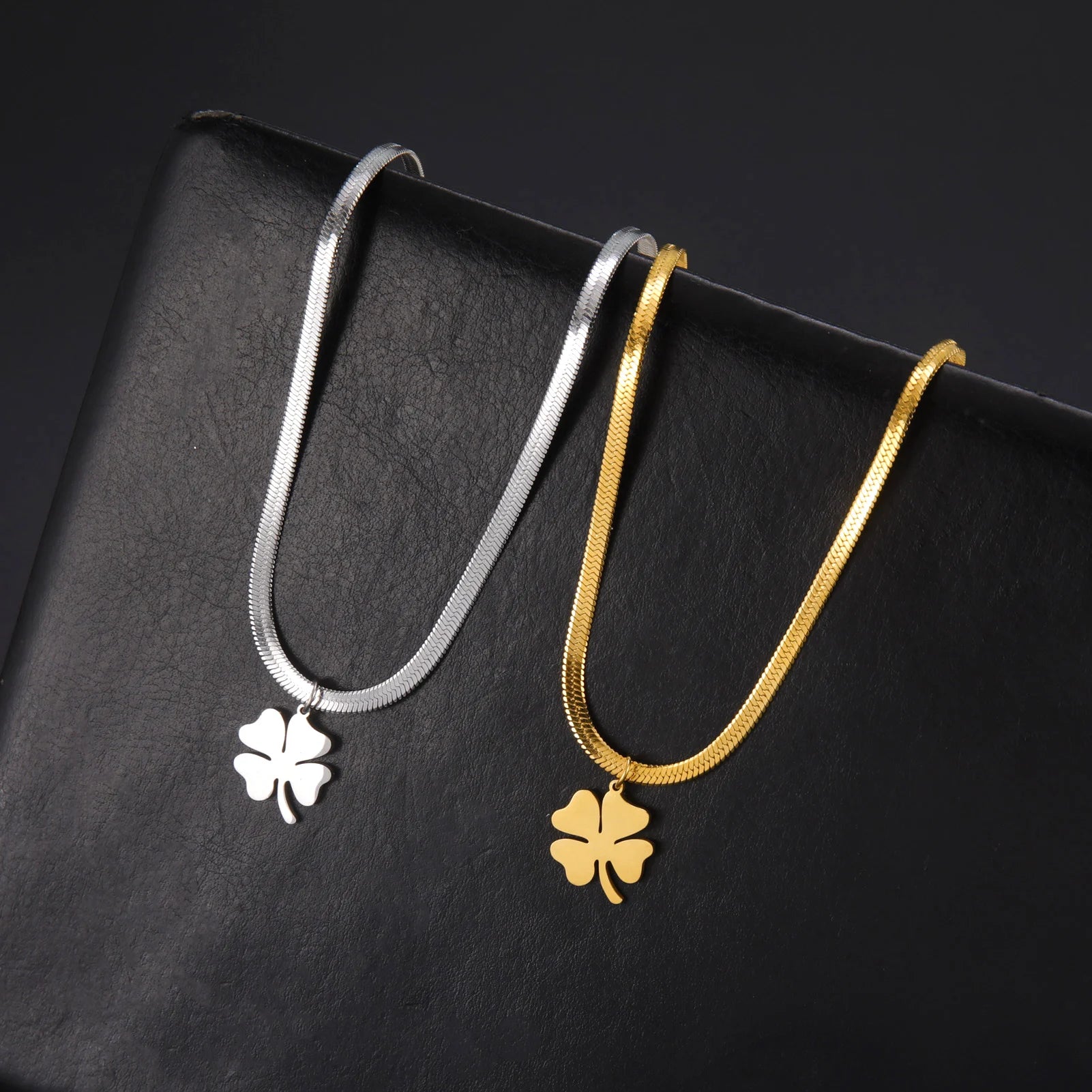 Gold and silver clover pendant necklaces displayed side by side on black leather