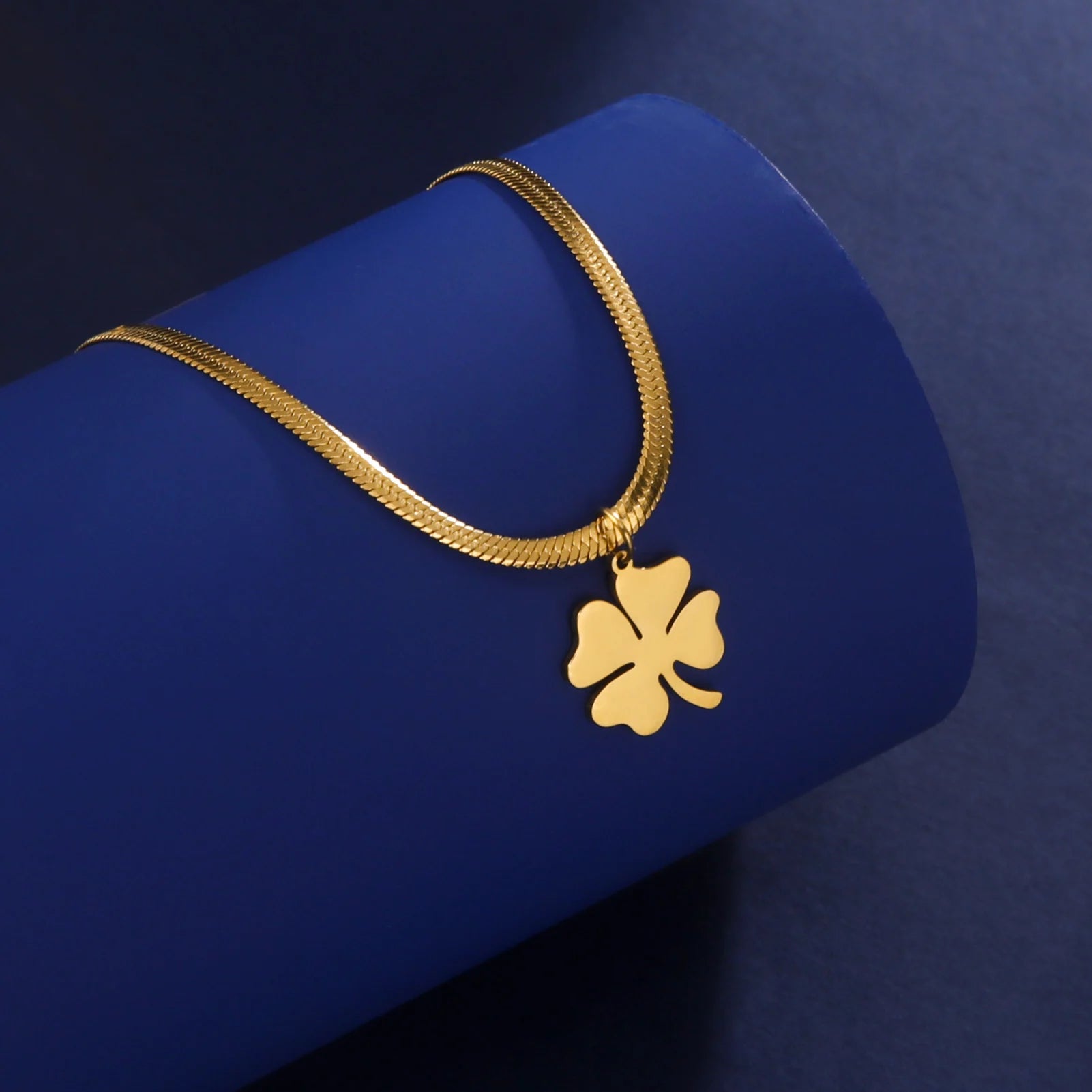 Gold clover pendant necklace displayed on blue cylindrical stand