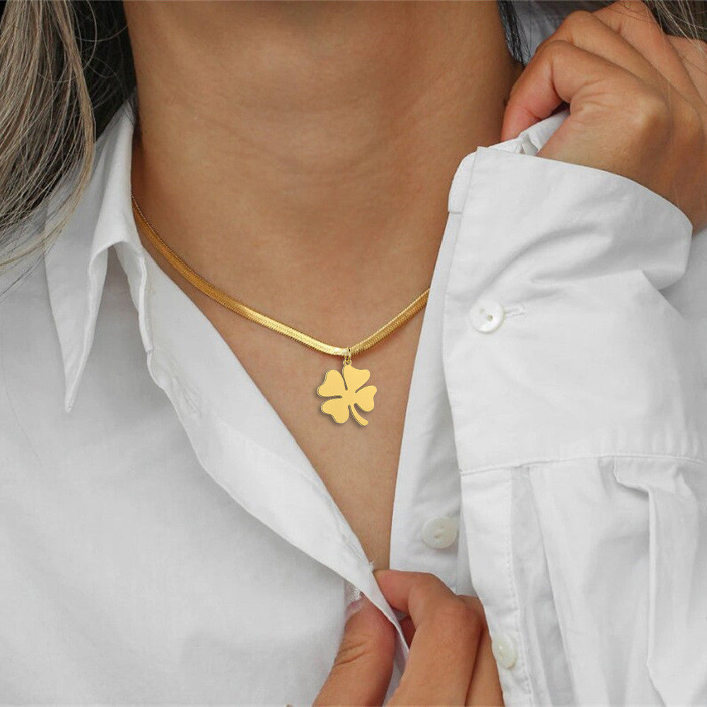 Gold clover pendant necklace worn with open white blouse, close-up chest view