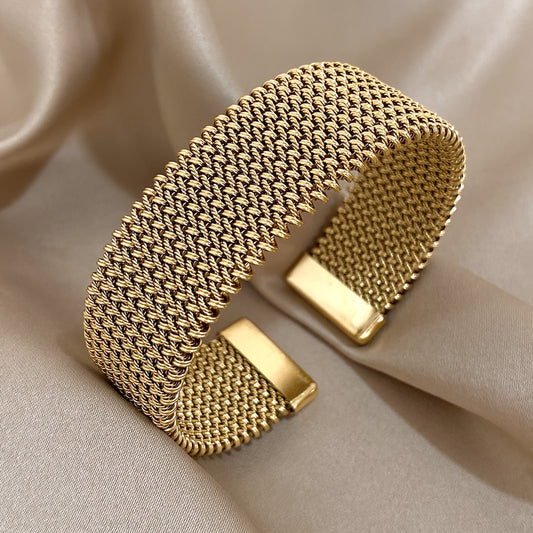Gold woven stainless steel bracelet on beige satin background, angled side view