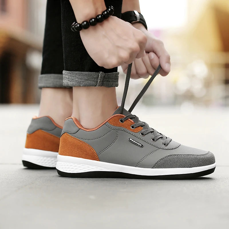 Grey and orange sneaker picked up by laces, street background