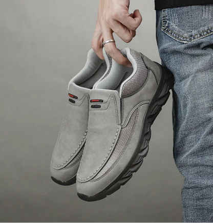 Hand holding pair of grey leather casual loafers against dark background