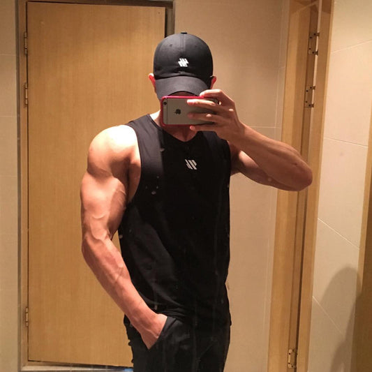 Man wearing black mesh tank top in bathroom mirror selfie with door background