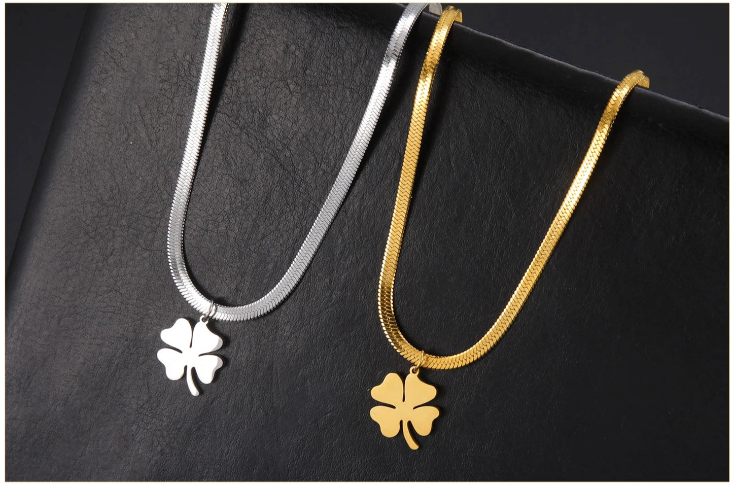 Pair of gold and silver clover necklaces displayed on textured leather surface