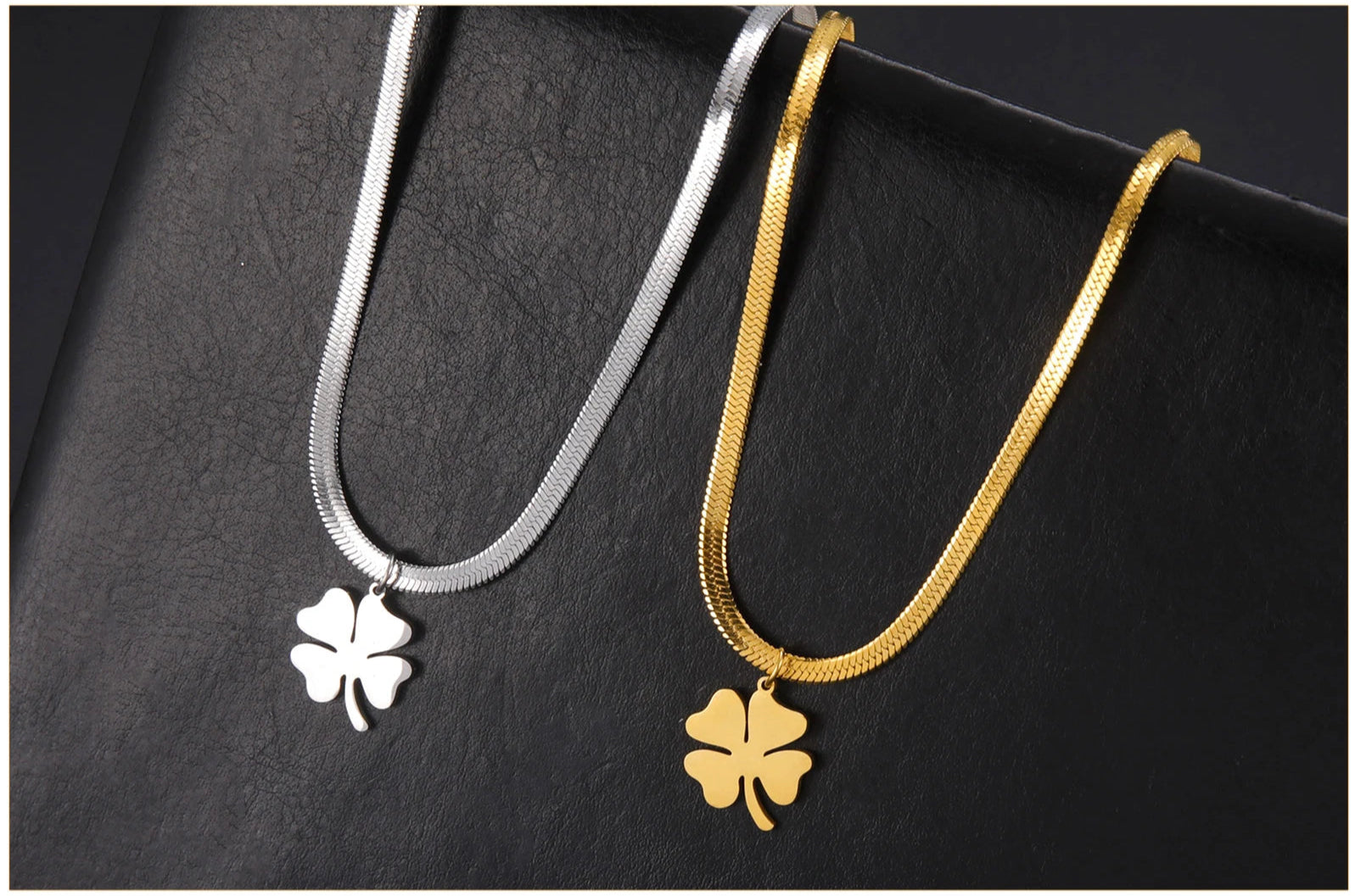 Pair of gold and silver clover necklaces displayed on textured leather surface